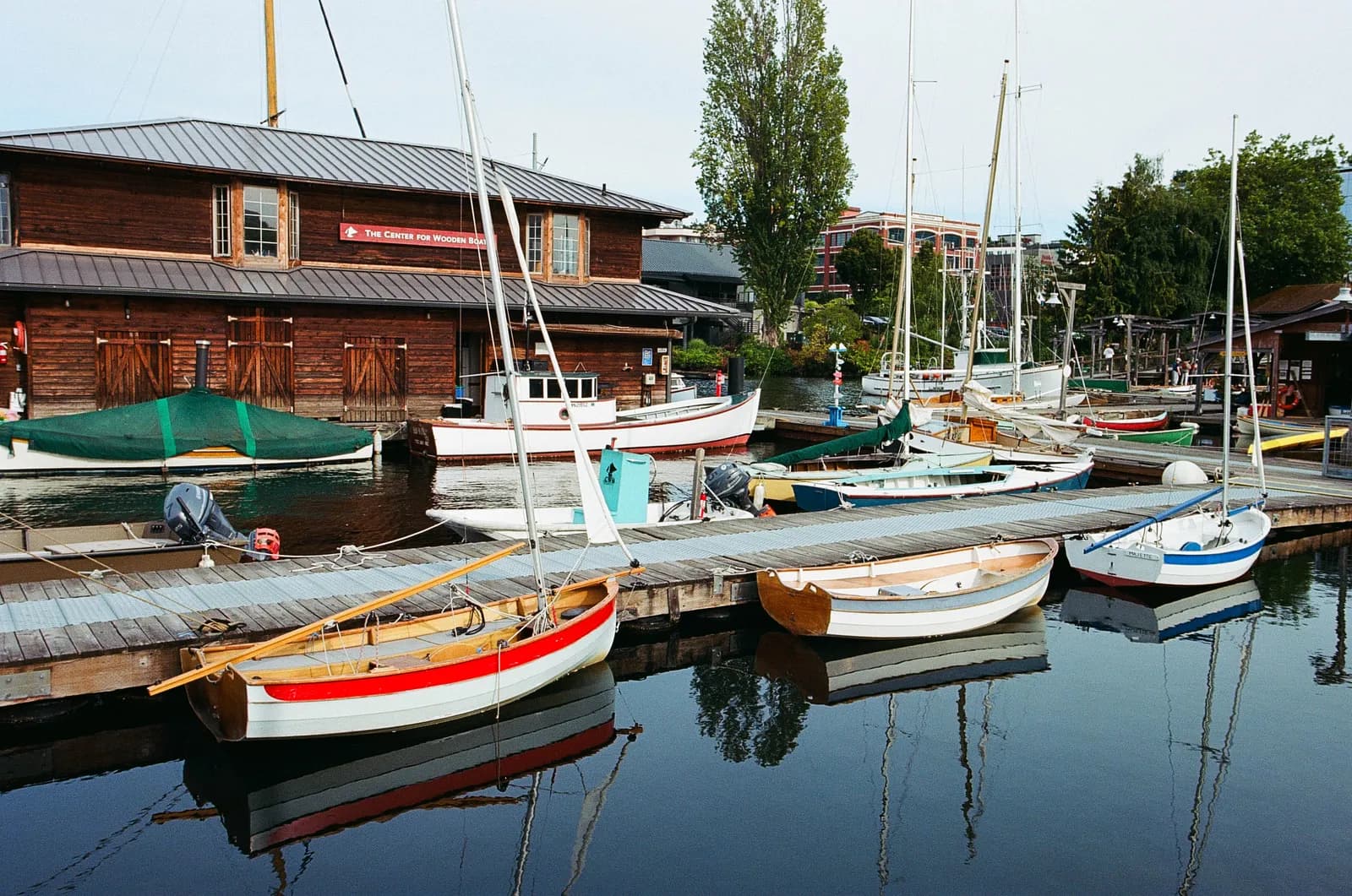 Wooden boats moored at a quiet harbor with reflections on calm water beside a weathered boathouse