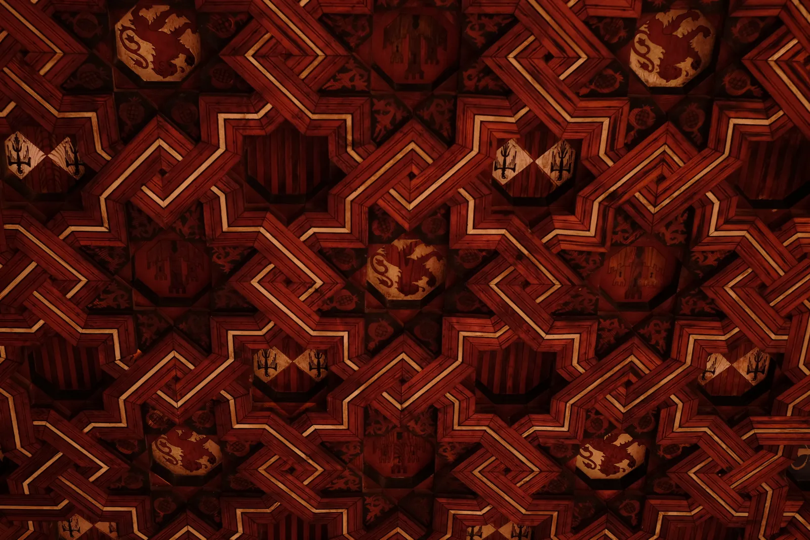 Interlocking geometric patterns in deep red and gold, representing the complex interdependence between GEO and SEO strategies where some patterns align and others conflict